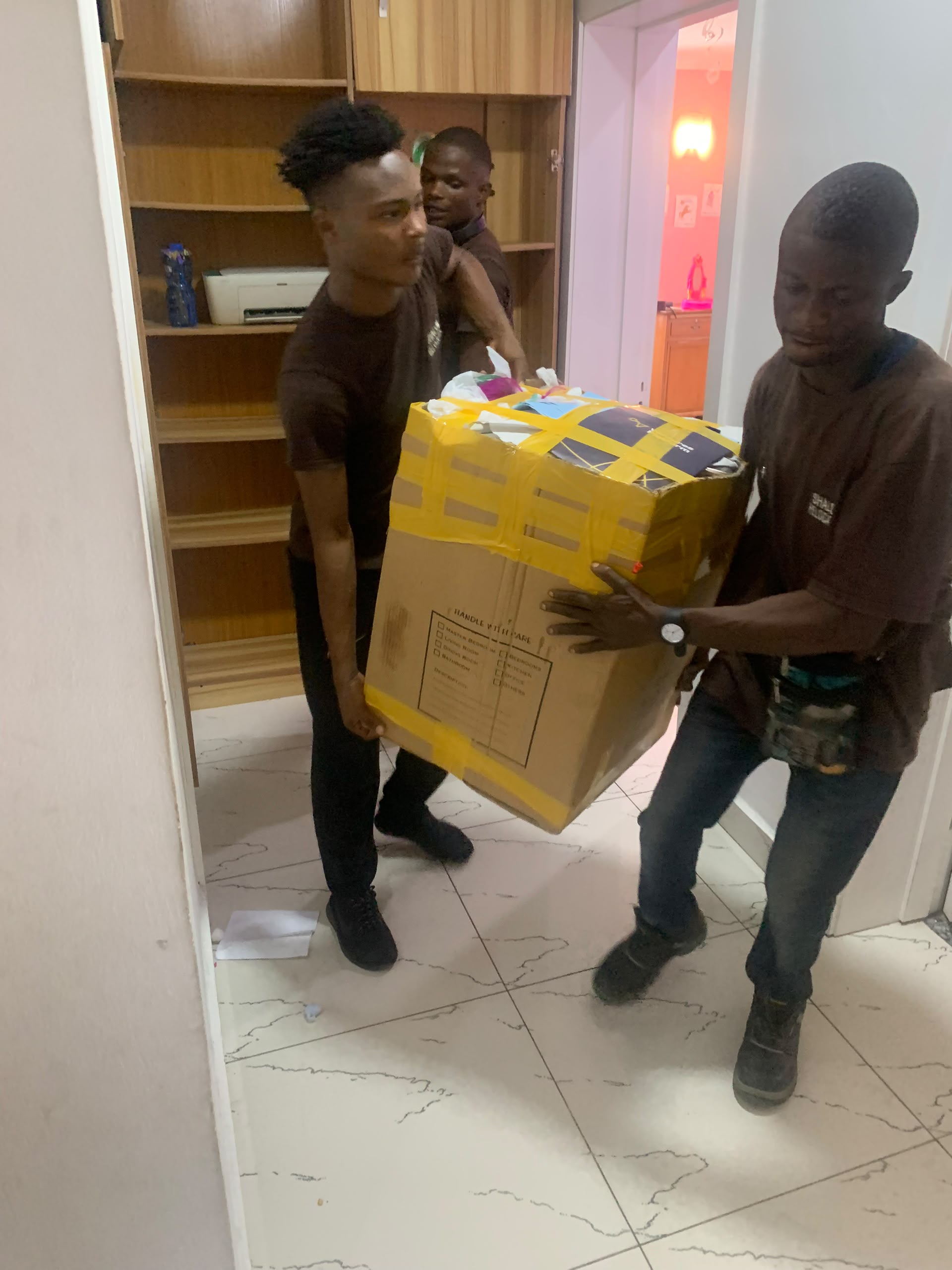 Shalom Relocation team members carrying a sealed box through a doorway.