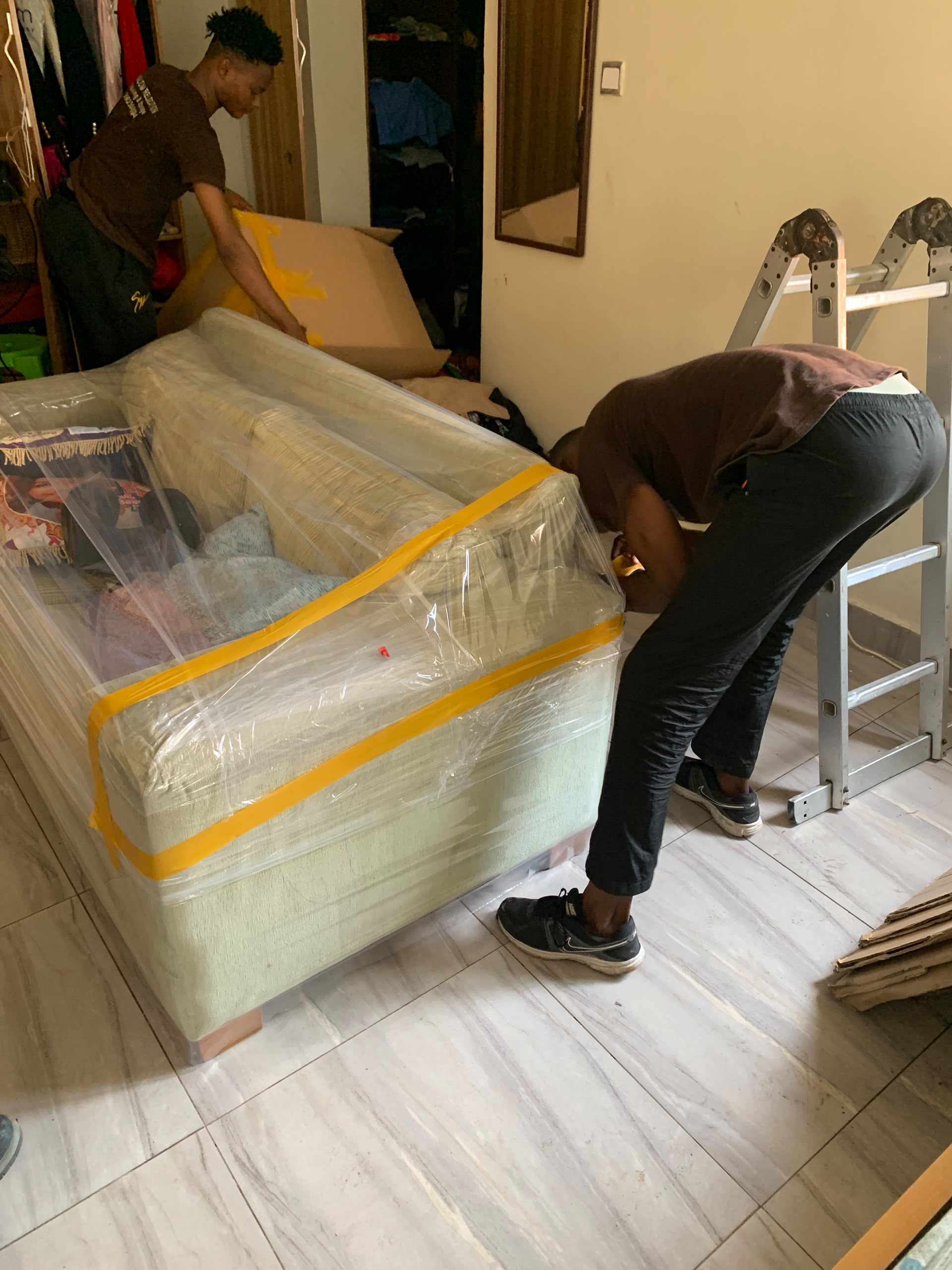 Movers handling a furniture piece protected with wrapping and yellow tape.